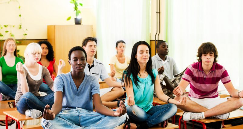 Group of teenagers sitting on the desk in lotus position.